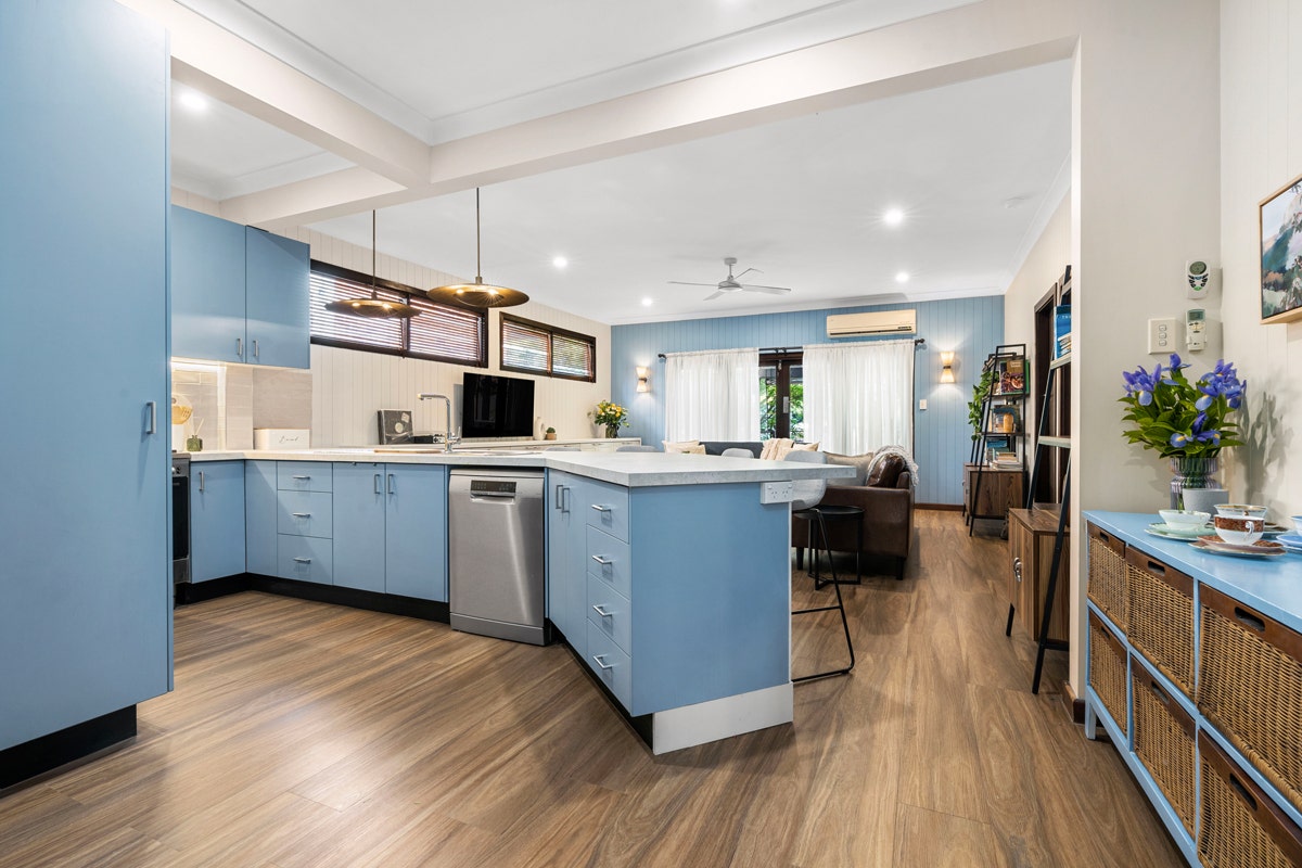 Modern kitchen with stainless steel appliances (sink, dishwasher, stove, oven). White cabinets, light hardwood floors, large window.