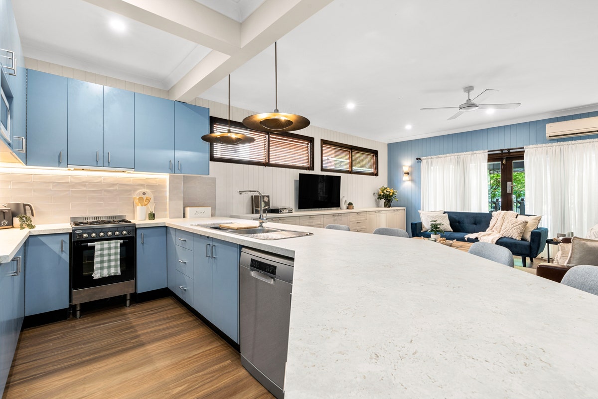 Modern kitchen with stainless steel appliances (sink, dishwasher, stove, oven). White cabinets, light hardwood floors, large window.