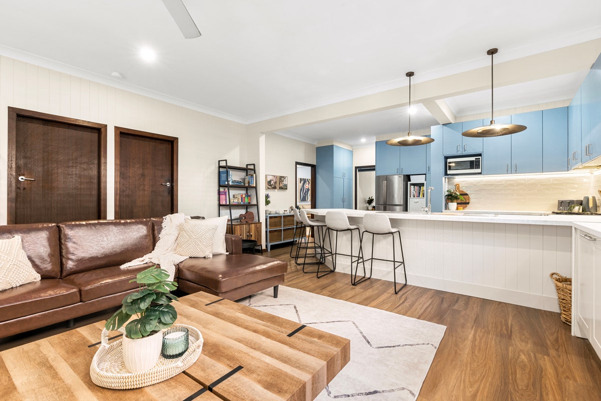 Living room with couch, coffee table, ceiling fan, and mounted TV connecting to the modern kitchen
