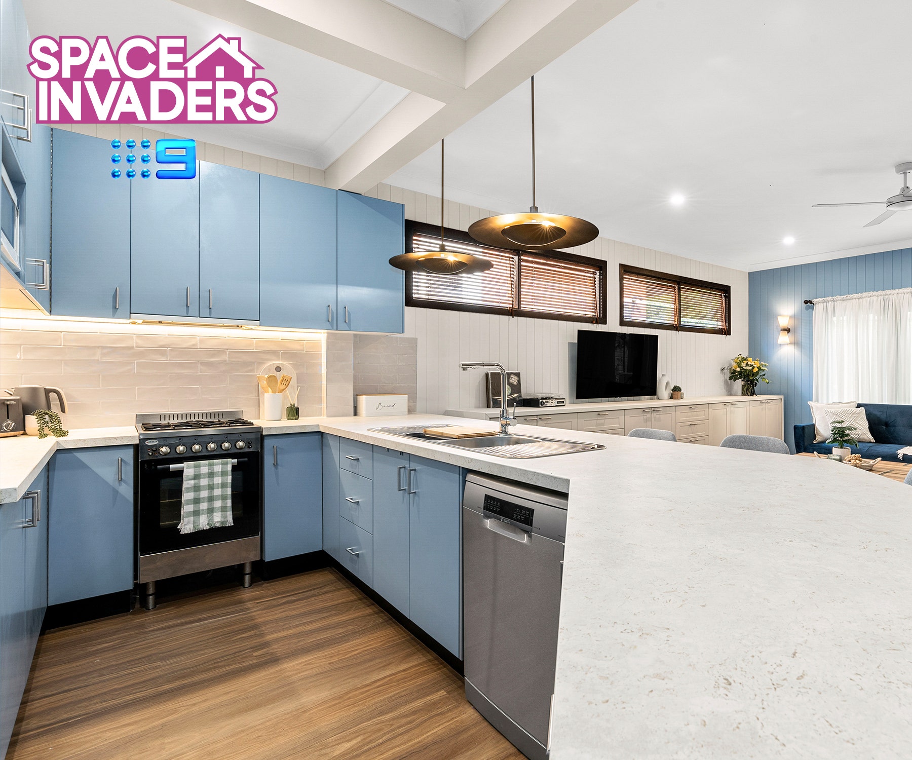 Modern kitchen with stainless steel appliances (sink, dishwasher, stove, oven). White cabinets, light hardwood floors, large window.